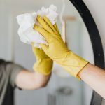 Close-up of a person cleaning a mirror with yellow gloves, focusing on hygiene and sanitation.